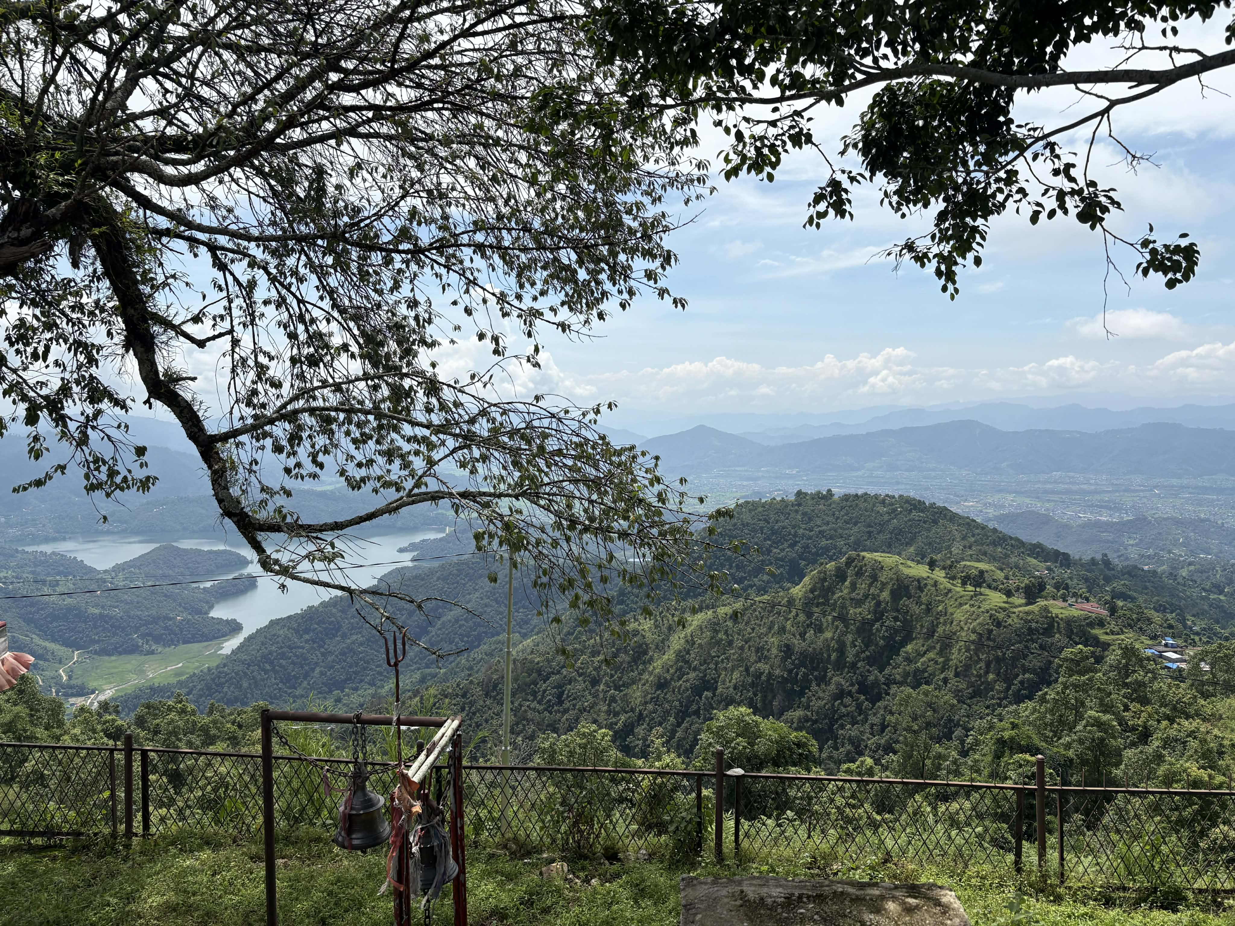 A scenic view from a high point, featuring a lush green landscape with rolling hills and a lake winding through the valley below. 