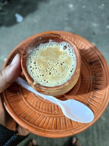 
A close-up of a hand holding a small clay cup of foamy tea on an orange clay plate.