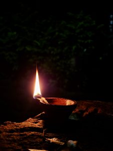 A single clay oil lamp burns brightly at night in Velliparamba, Kozhikode. The warm flame lights up the pot and the nearby surface, creating a cozy and peaceful feeling in the quiet darkness. 