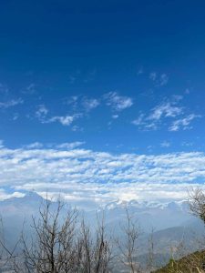 Clear sky over Himalayan mountain range with scattered clouds and foreground dry branches creating a natural, serene landscape view.