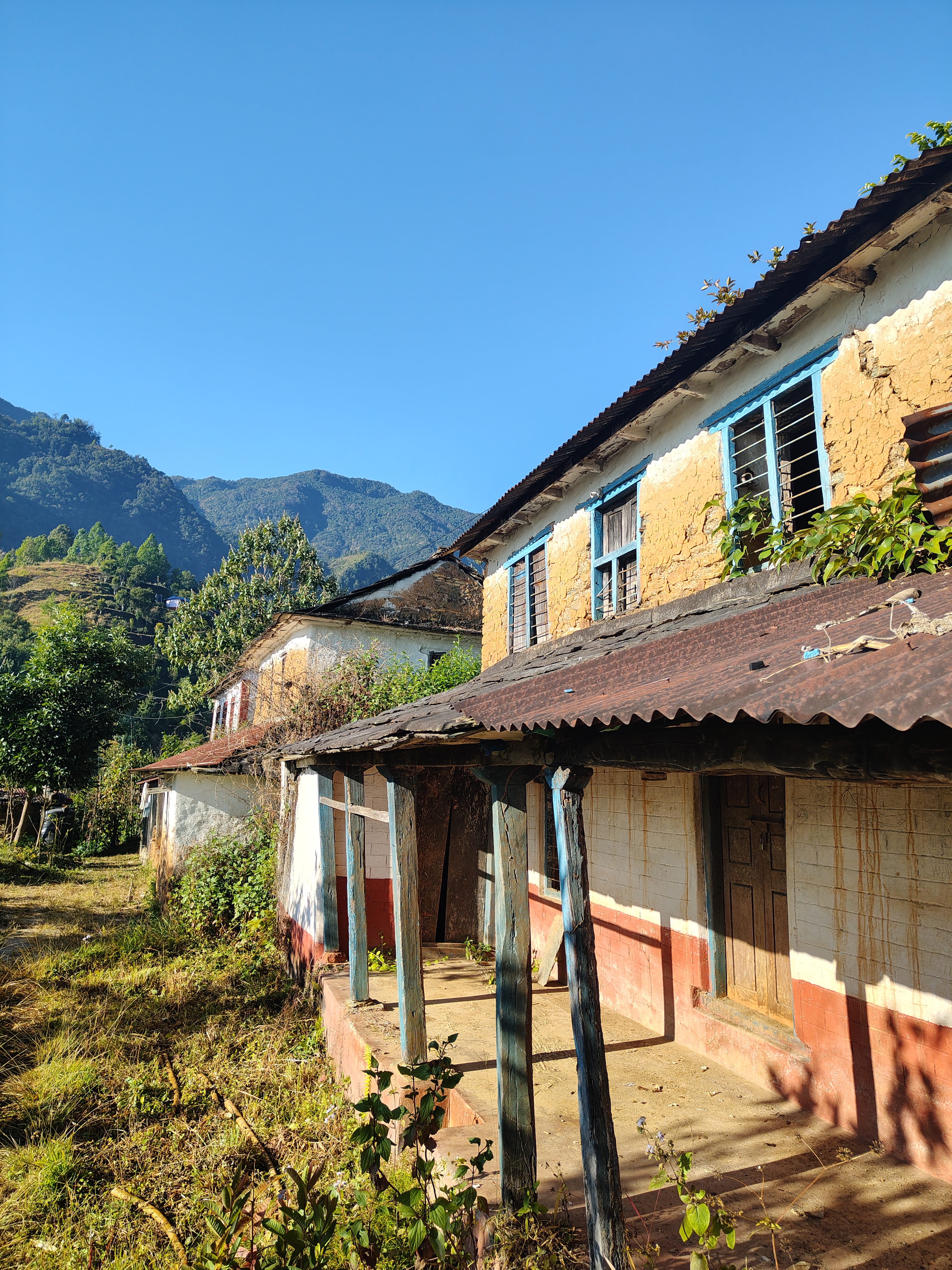 A picturesque scene of an old, rustic house with a weathered façade in earthy tones, featuring blue window frames and a sloping roof. 