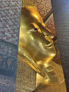 Reclining Buddha statue at Wat Pho temple in Bangkok, covered in gold leaf, viewed from the side inside the temple hall.