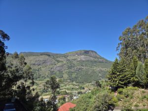 A wide view of green mountains under a clear blue sky, with terraced fields, trees, and a few buildings in the valley below.