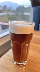 A clear glass filled with amber-colored beer, topped with a creamy white foam, placed on a wooden table.