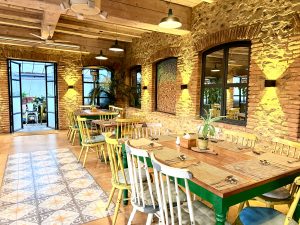 A cozy dining area featuring rustic stone walls, wooden beams, and multiple dining tables with colorful chairs.