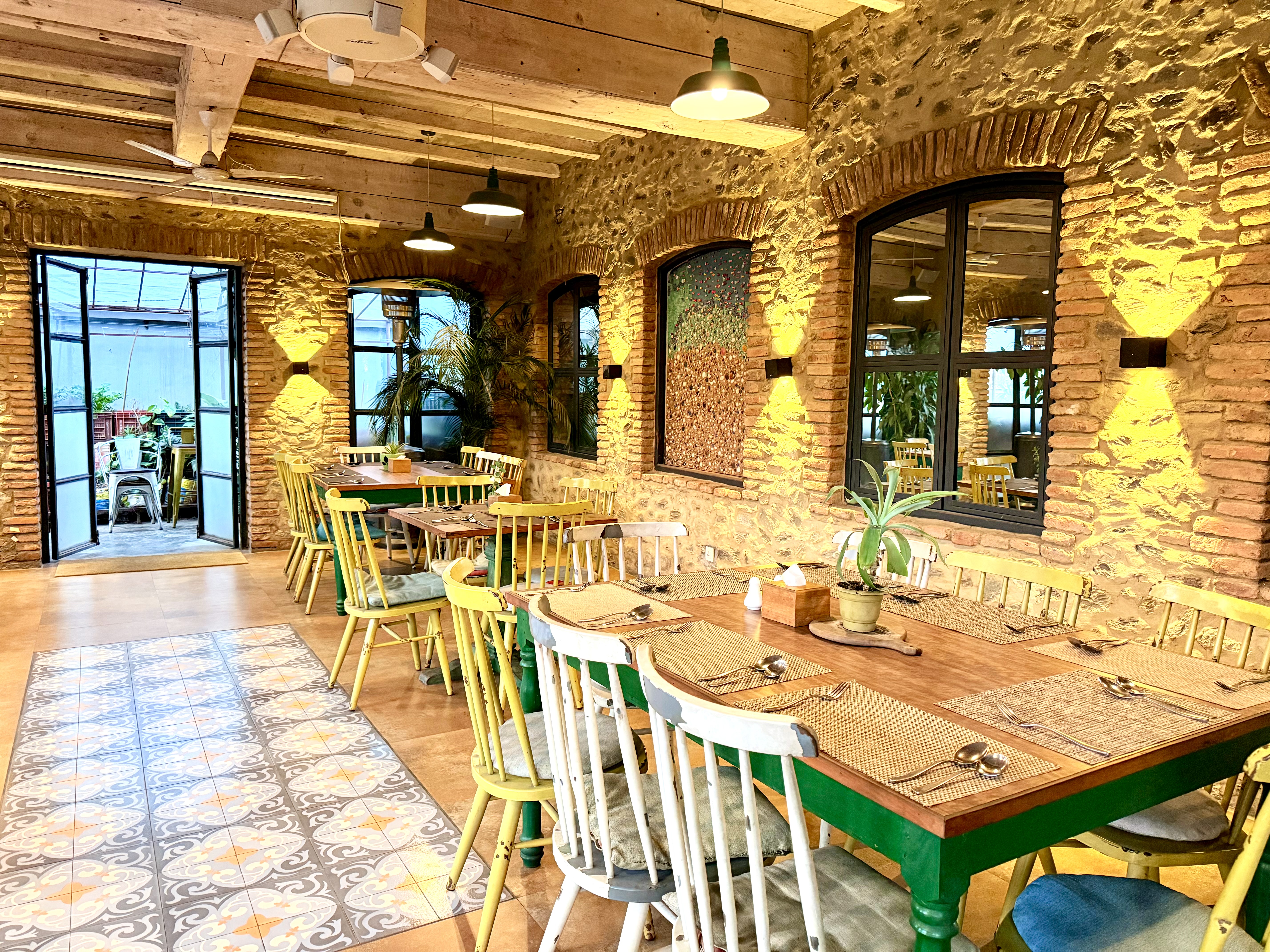 A cozy dining area featuring rustic stone walls, wooden beams, and multiple dining tables with colorful chairs.