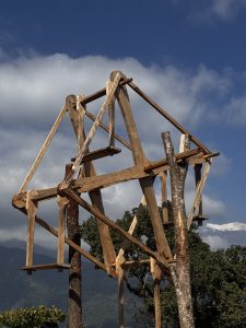 A wooden structure called Rote Ping stands in front of mountains under a cloudy sky.
