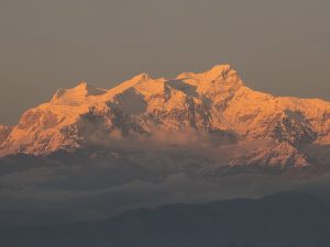 A stunning view of snow-capped mountains at sunset, with the peaks illuminated in a warm, golden light.