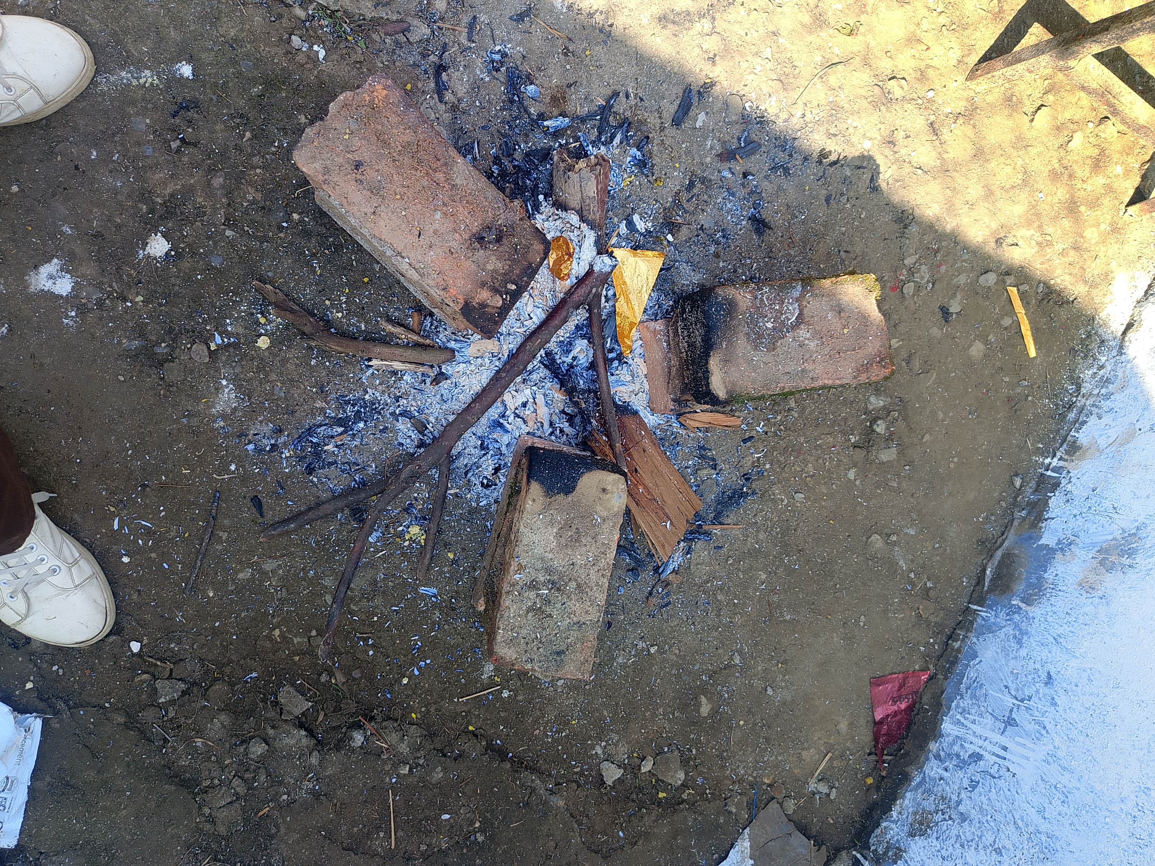 A small fire pit made of several bricks and sticks, surrounded by ashes and remnants of burnt wood. 