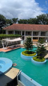 A calm swimming pool with clear turquoise water, surrounded by green plants and small tree islands, in Sreemangal, Sylhet, Bangladesh.