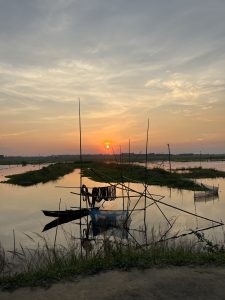 A fishing boat rests on the sandy shore, with gentle waves lapping at its hull under a clear blue sky.