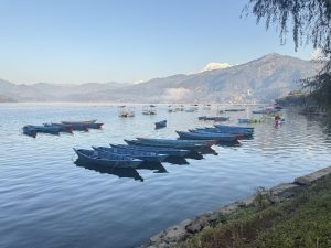 A serene lakeside scene featuring several colorful wooden boats floating on calm water.
