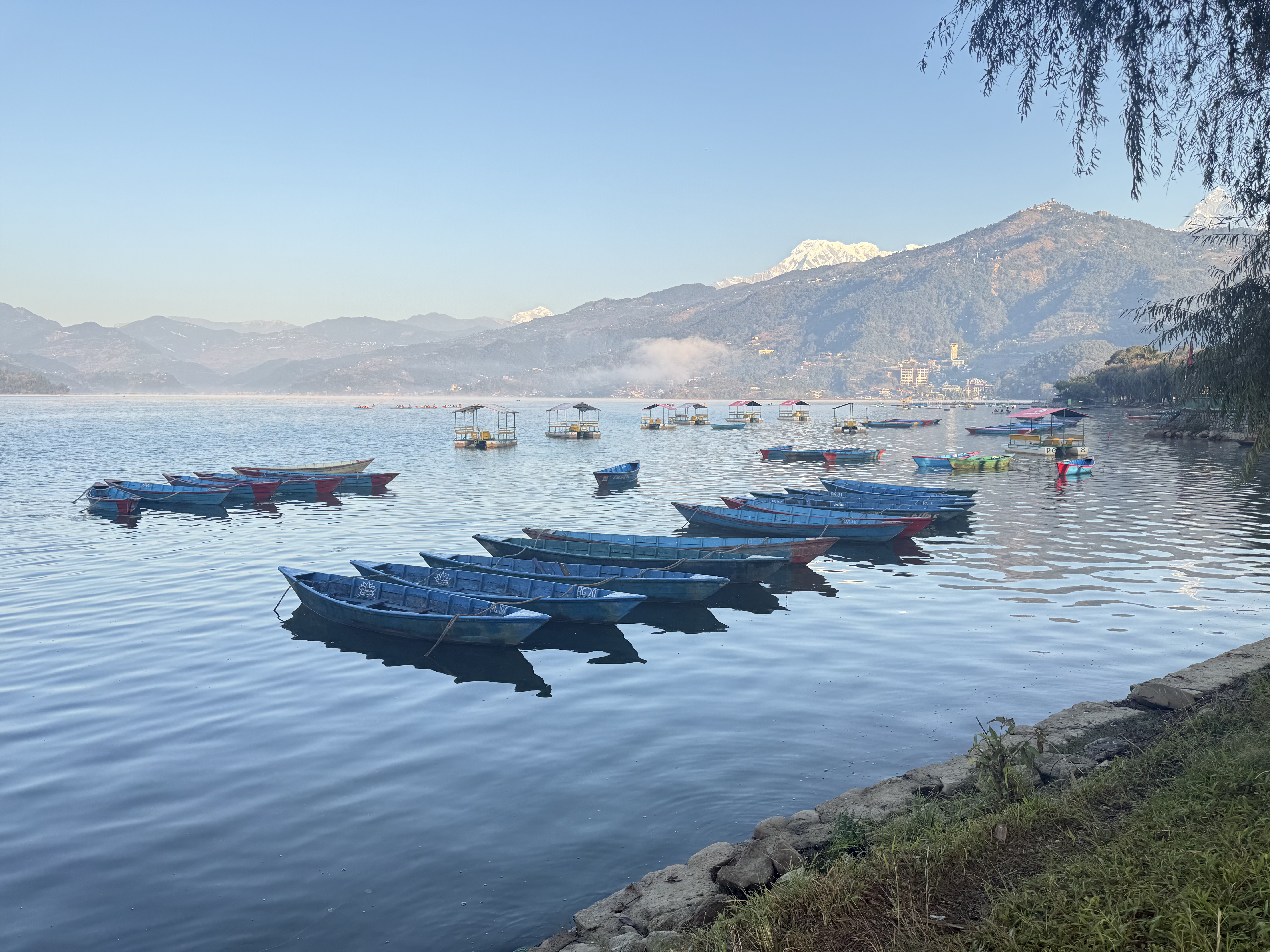 A serene lakeside scene featuring several colorful wooden boats floating on calm water.
