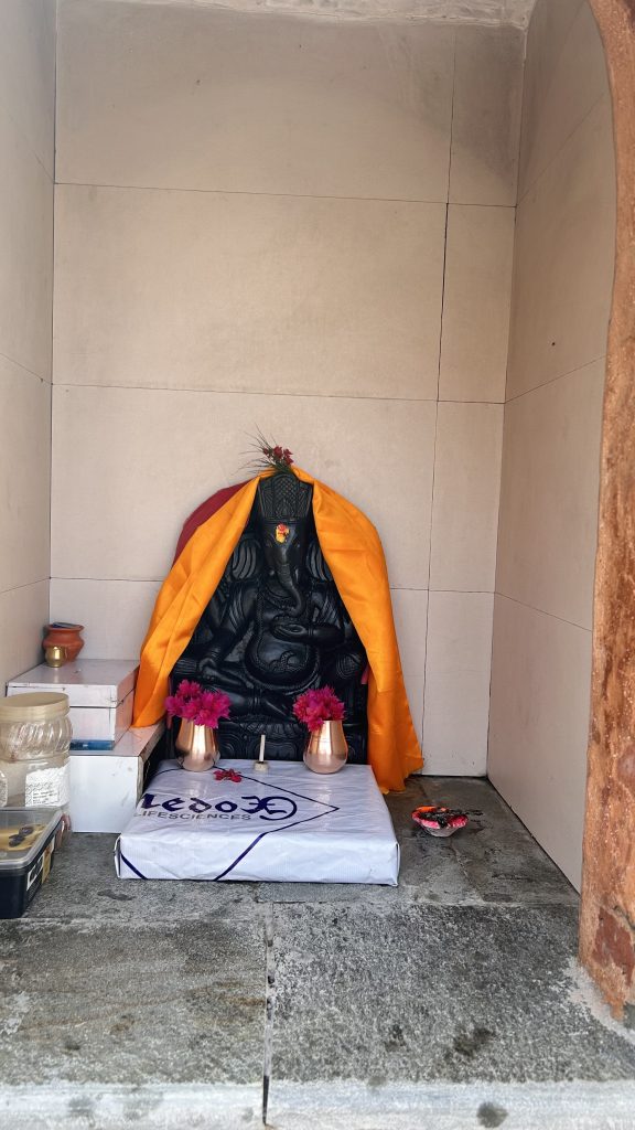 A black stone statue of Ganesha, adorned with an orange cloth and a red shawl, is situated in a small alcove.