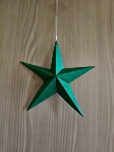 A green paper star decoration suspended on a thread, photographed against a wooden surface. The neat folds and rich colour reflect simple festive creativity. This minimal Christmas decoration was captured in Kozhikode, Kerala. 
