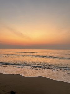 Calm ocean waves gently washing onto a sandy beach at sunset in prachuap khiri khan, thailand, with a soft pastel sky in shades of orange and pink reflecting on the sea.