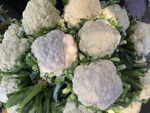 Fresh cauliflower heads with vibrant green leaves, glowing in sunlight and conveying freshness.
