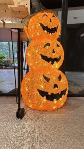 A decorative display featuring three stacked, illuminated orange pumpkins with carved face