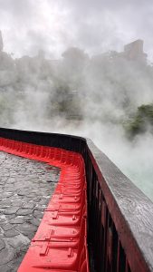 A misty landscape featuring a stone path curving alongside a wooden railing with bright red barriers.