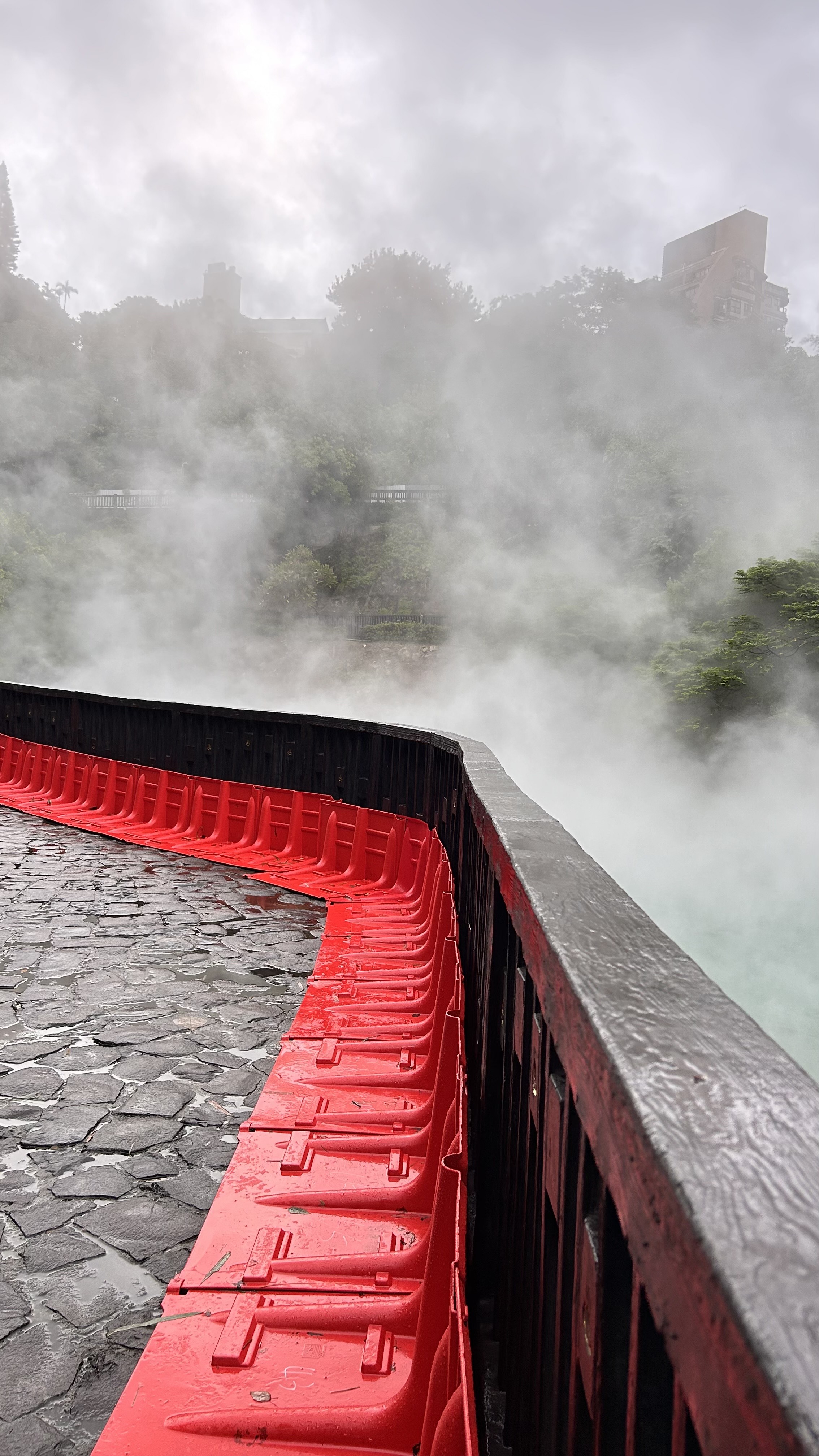 A misty landscape featuring a stone path curving alongside a wooden railing with bright red barriers.