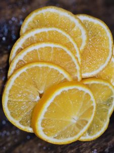 Fresh orange/citrus slices are arranged neatly, showcasing their bright yellow-orange color and juicy texture, captured in a simple indoor setup (from Perumanna, Kozhikode) that highlights the fruit's natural freshness and vibrant look.