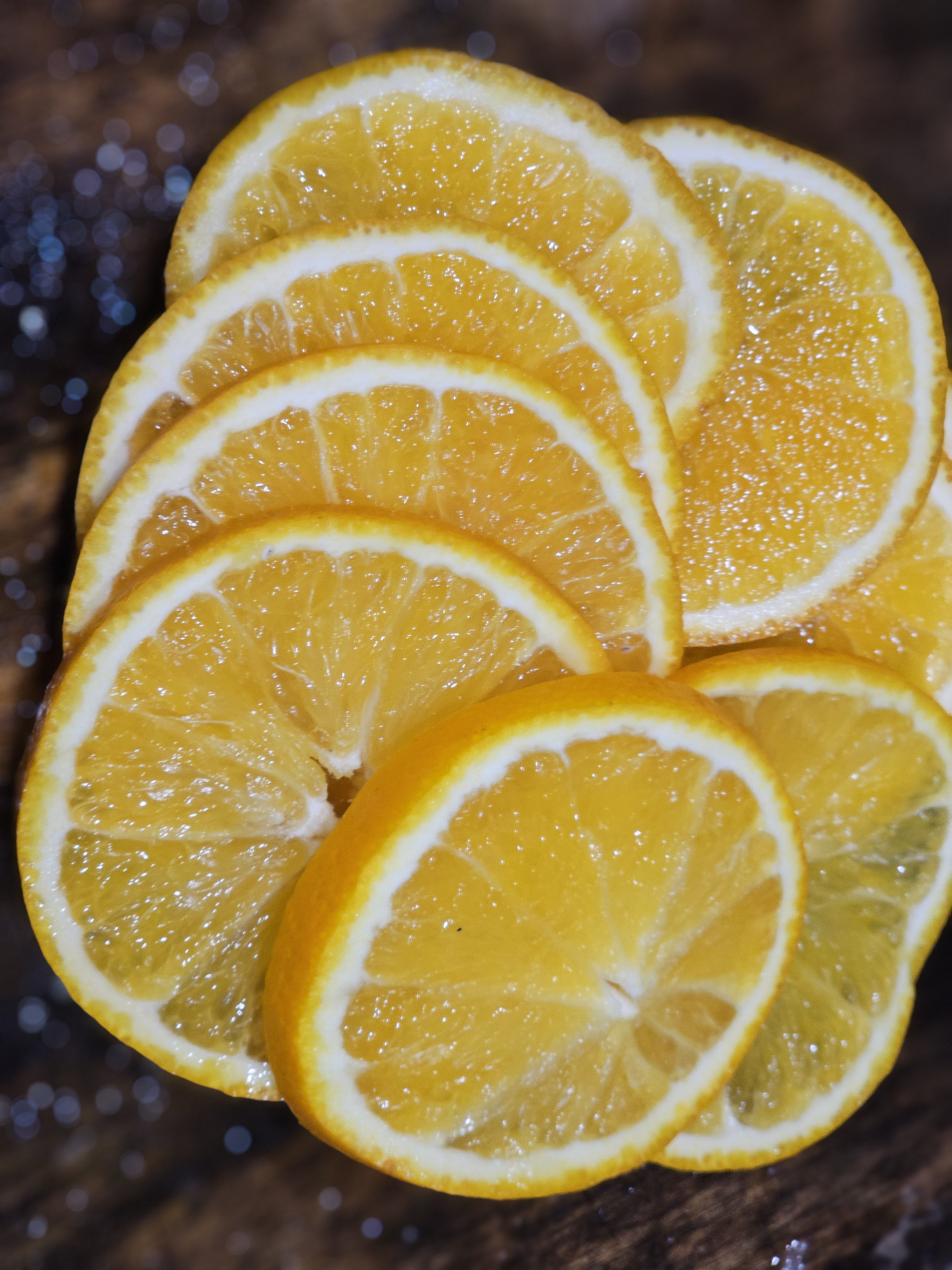 Fresh orange/citrus slices are arranged neatly, showcasing their bright yellow-orange color and juicy texture, captured in a simple indoor setup (from Perumanna, Kozhikode) that highlights the fruit's natural freshness and vibrant look.