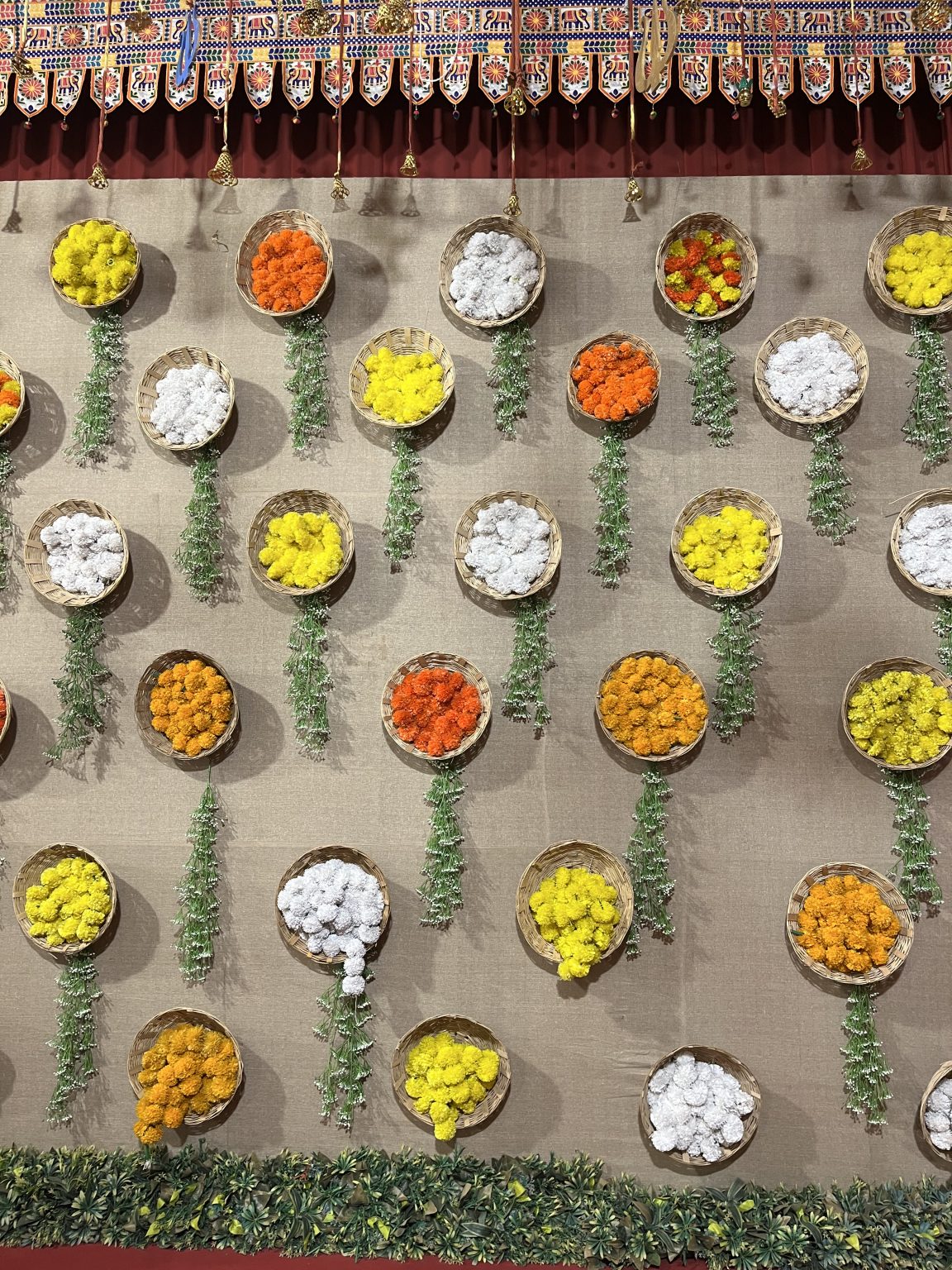 A decorative wall with circular baskets filled with vibrant artificial flowers in yellow, orange, white, and red.