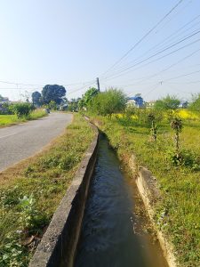 A rural scene depicting a narrow water channel running parallel to a road. 