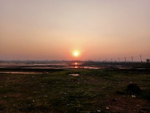 A calm sunset over water and grassy fields in Brahmanbaria, Bangladesh.