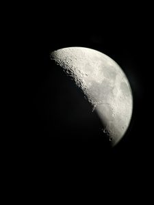Detailed view of the Moon in partial phase with visible craters and rugged surface against a black night sky.
