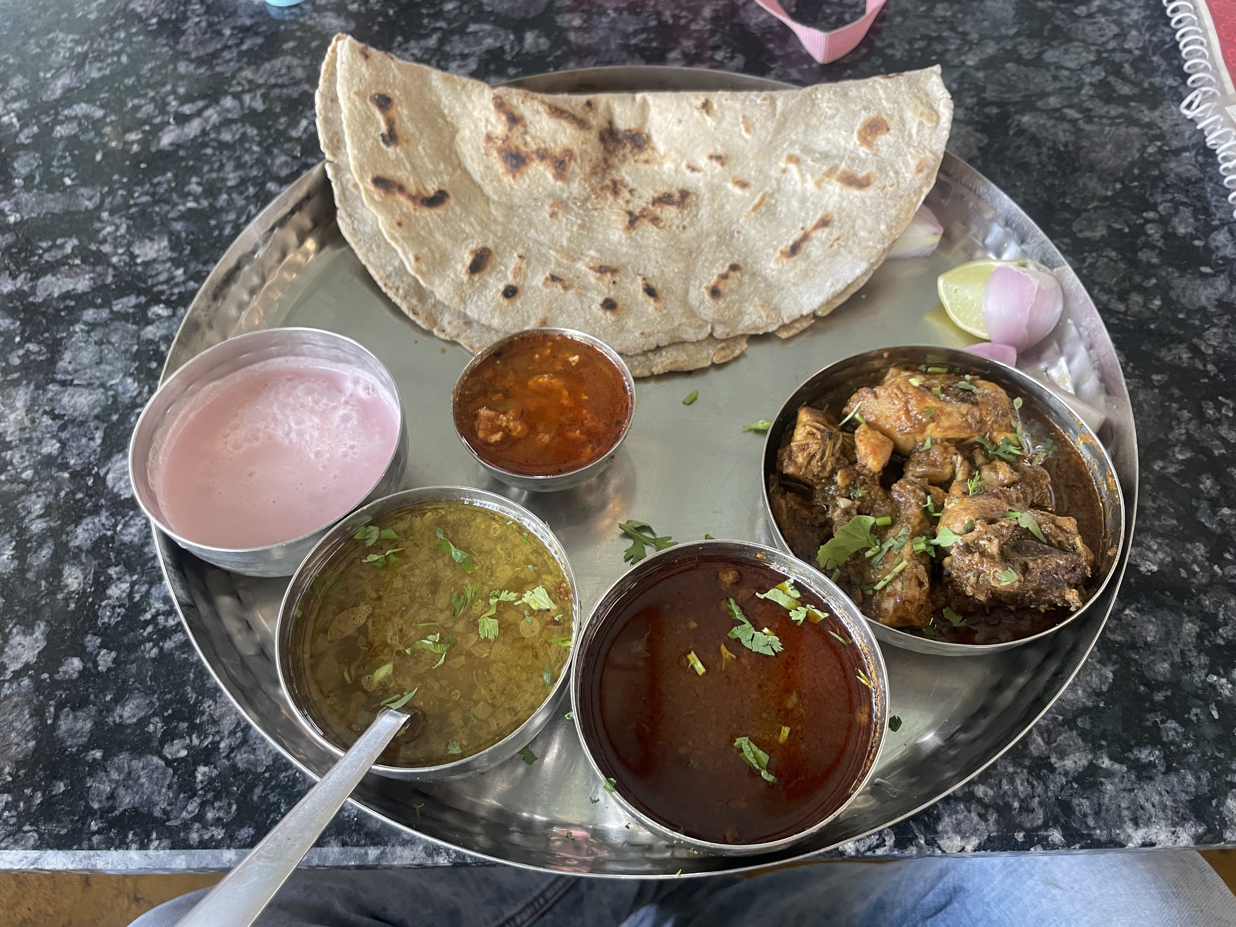 A stainless steel plate holds an assortment of Indian dishe