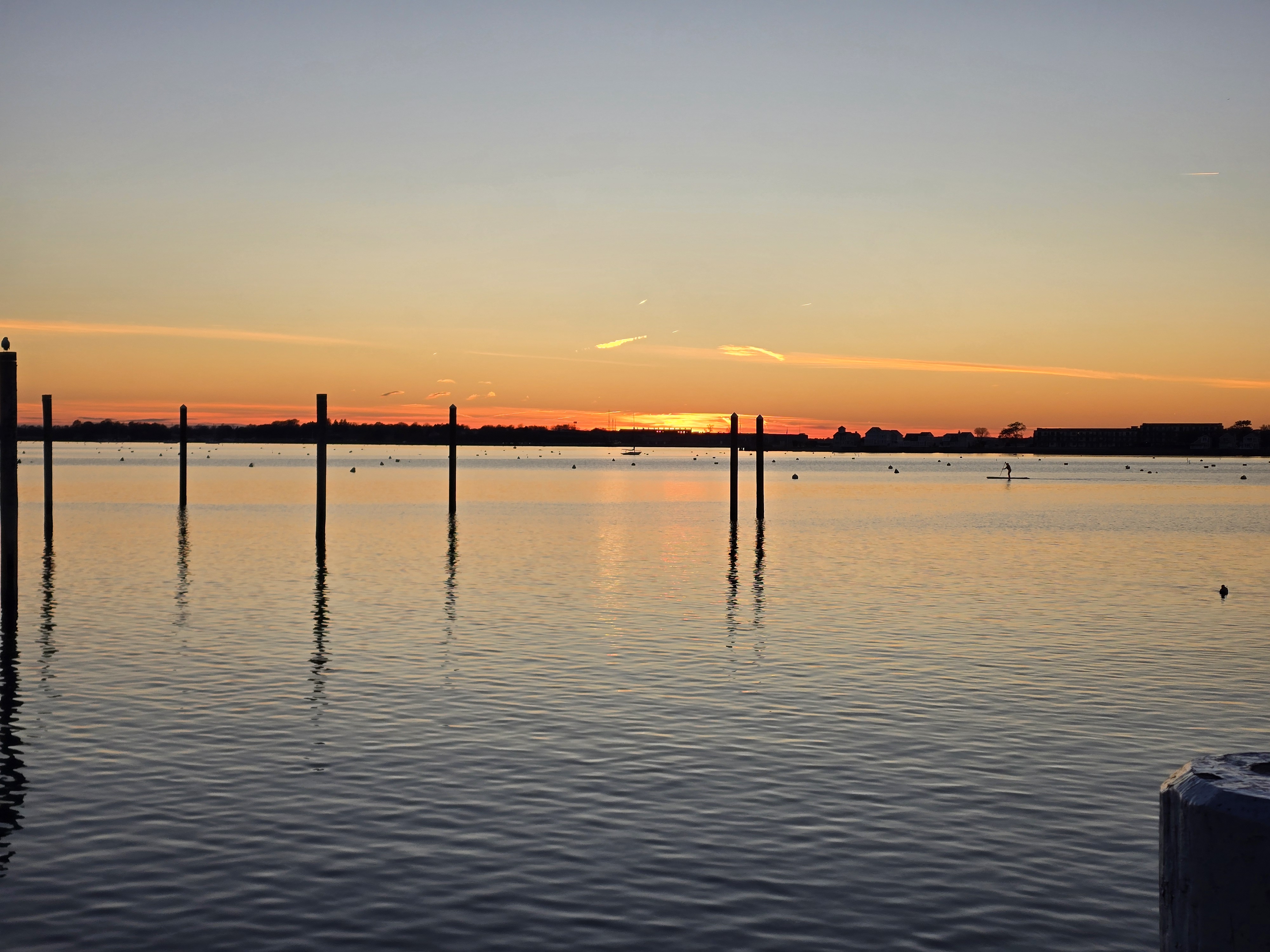 A serene sunset over calm waters with a line of wooden posts in the foreground in Newport, Rhode Island.