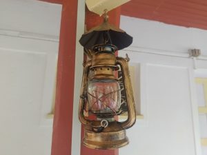 
A vintage oil lantern hangs from a ceiling, featuring a metallic body with a brass-like finish