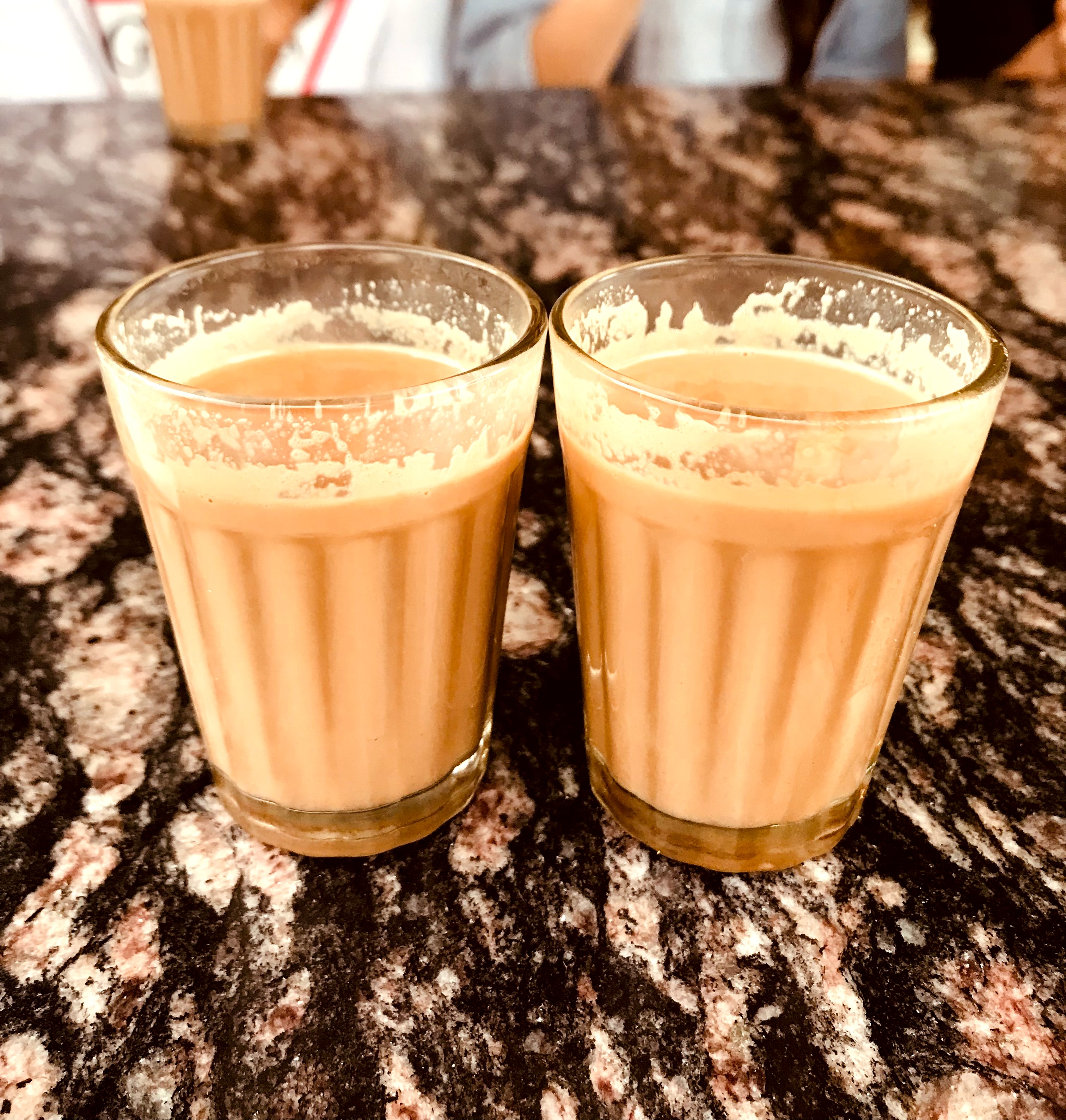 Two glasses of milk tea on a dark granite countertop.