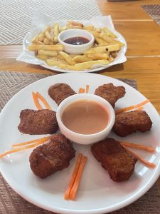 A plate with six golden-brown chicken nuggets arranged in a circular pattern around a small bowl of dipping sauce, garnished with thin strips of orange carrot.
