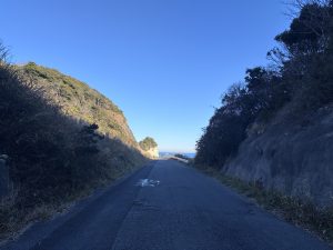 A narrow, paved road leads toward a distant viewpoint, flanked by steep, green hills on both sides.