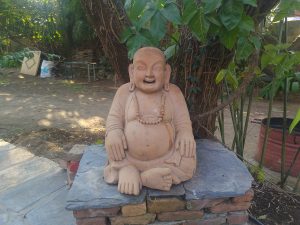 A seated laughing buddha with a round belly, simple robe, and beaded necklace.