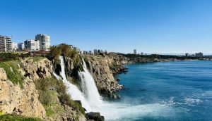 A picturesque coastal scene featuring cascading waterfalls flowing over rocky cliffs into a serene, blue sea.