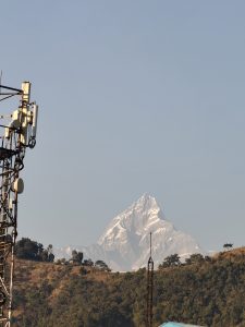 A snow-capped mountain peak rises prominently against a clear blue sky, with rolling hills and trees in the foreground.
