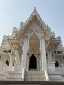 A beautifully detailed white temple structure with intricate architectural designs, featuring ornate gables and stair steps leading up to a central entrance.