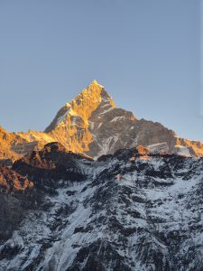 Machhapuchhre (Fishtail) glowing warmly at sunrise amid rugged, rocky terrain.