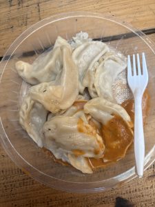 A clear plastic container filled with several dumplings, some sitting on a small pool of orange sauce. 