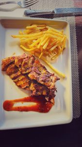 A plated dish featuring grilled, seasoned meat alongside a serving of golden, crispy French fries.
