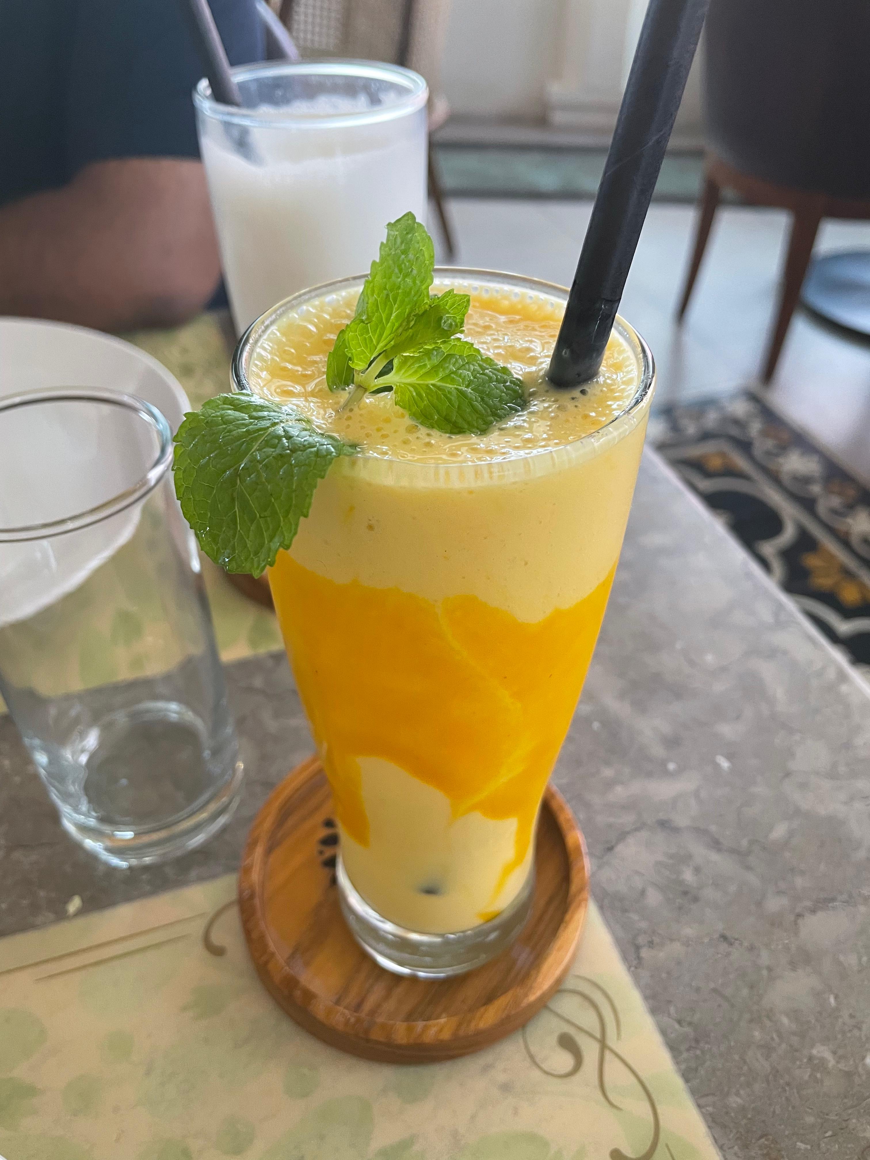 A tall glass filled with a vibrant yellow smoothie, topped with fresh mint leaves and a black straw.