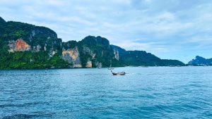 Turquoise sea in the foreground with steep limestone cliffs covered in greenery along the coast in Phi Phi Island, Thailand
