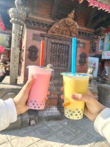 Two hands are holding colorful bubble tea drinks&mdash;one pink with red straw and the other yellow with blue straw. 