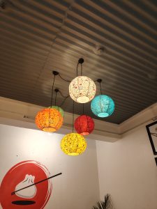 A ceiling with six colorful hanging lanterns in various shapes, including red, orange, yellow, white, and turquoise.