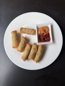 A white plate holds several golden-brown, crispy spring rolls arranged neatly.