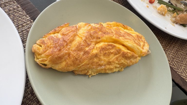 A perfectly cooked, golden-brown folded omelet served on a light green ceramic plate.