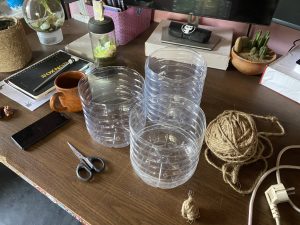 A wooden desk with containers, twine, scissors, a phone, a mug, a notebook, and small plants.